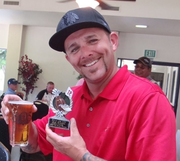 event winner smiling, holding a beverage and his trophy