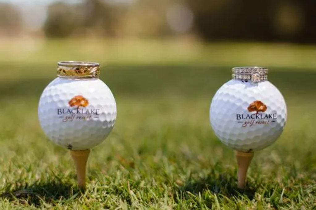 Wedding rings sitting on top of side-by-side golf balls on golf tees on golf course